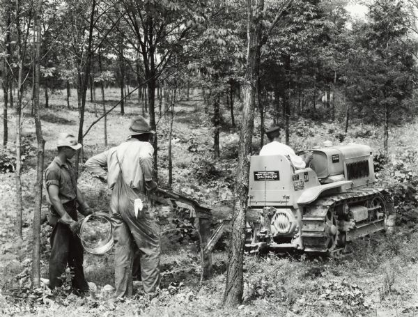 Three men laying wire in a forested area for W.H.A.S Radio. One of the men is operating an International T-20 TracTracTor (crawler tractor).