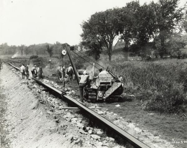 T-20 and Sideboom Workers lay a pipeline in a field using an International T-20 TracTracTor (crawler tractor) and sideboom. Original caption states: "Jones & Hannahan."