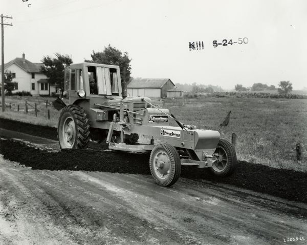 Man smoothing a road with a Meili-Blumberg (MB) Model 10 power grader attached to an International MD tractor. According to the original caption, the power grader had a 12-foot blade and was owned by Calumet County.