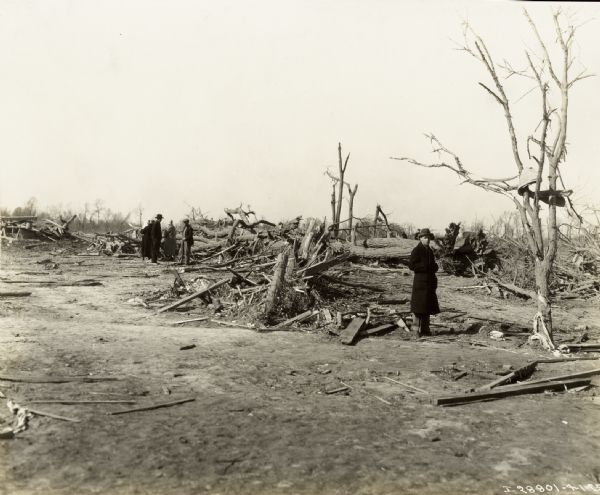 Men standing in a field with trees and buildings damaged by the "tri-state tornado."
