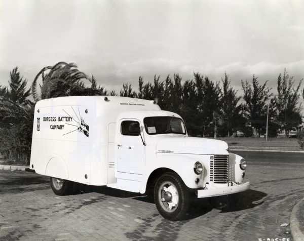 An International truck used by the Burgess Battery Company is parked on a drive with trees and road in the background.