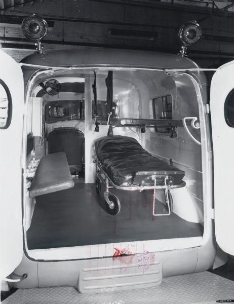 Interior view of an International KB-2 panel truck converted into an ambulance. The original caption reads: "These trucks equipped with Baumgardner cots, overhead stretcher, medicine cabinet, and ventilating unit. These trucks were made for shipment to Siam."
