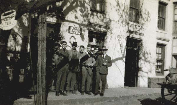 Six male staff members standing on the sidewalk in front of a Deering dealership in South Africa. The "Deering" brand was sold by International Harvester Company.