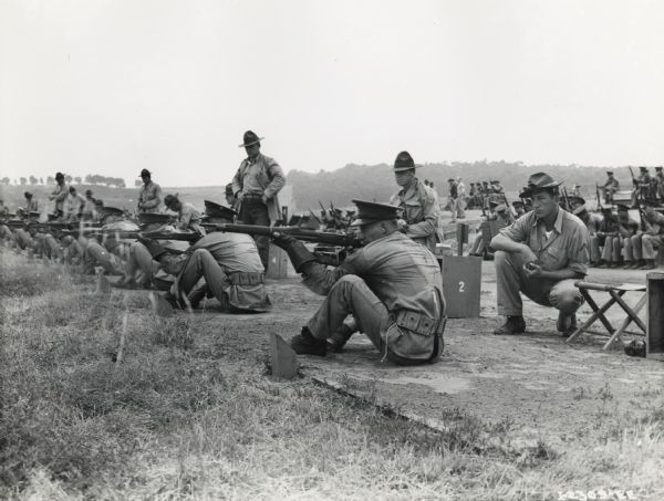 Large group of marines are outdoors firing from a sitting position at a firing range, possibly at a Marine Corps firing range at La Jolla, California.