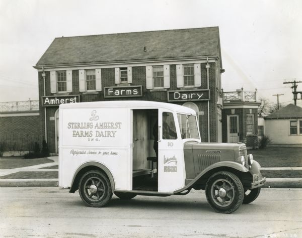 Sterling Amherst Farms Dairy Truck A man driving an International truck down a road in front of the Sterling Amherst Farms Dairy building.