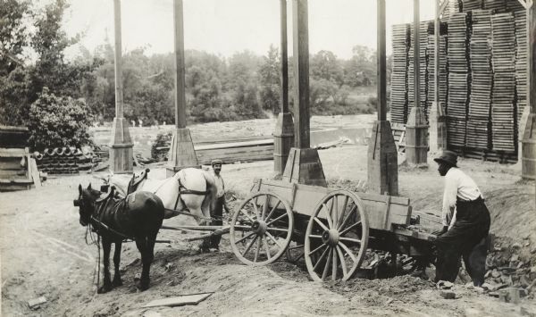 Two men with a horse-drawn wagon loaded with lumber at a construction site.