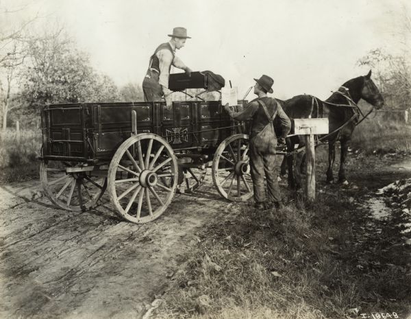 Man Delivering Mail with Horse and Wagon A man stands in the back of a horse-drawn Weber wagon to deliver mail to rural resident, possibly a farmer, standing by mailbox.