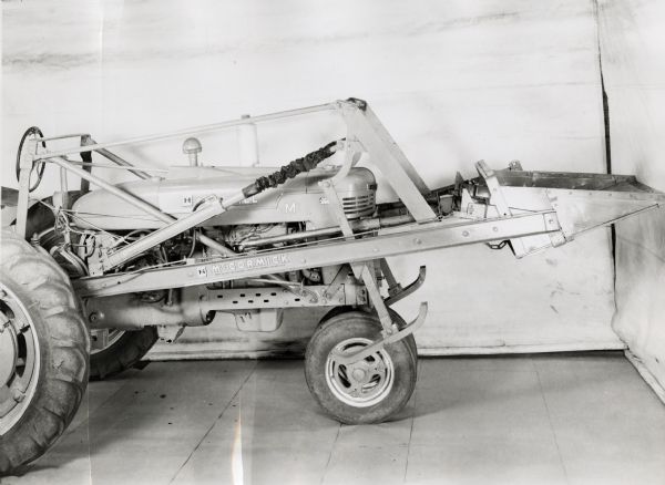 Engineering photograph of a Farmall M tractor with mounted #31 power loader on display in front of a white backdrop. The machinery may have been experimental.