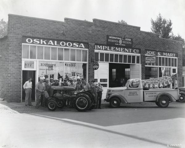 Exterior view of the Oskaloosa Implement Company, an International Harvester dealership. A group of men and young boys pose near a Farmall A Tractor, and on the right is an International D-2 truck.