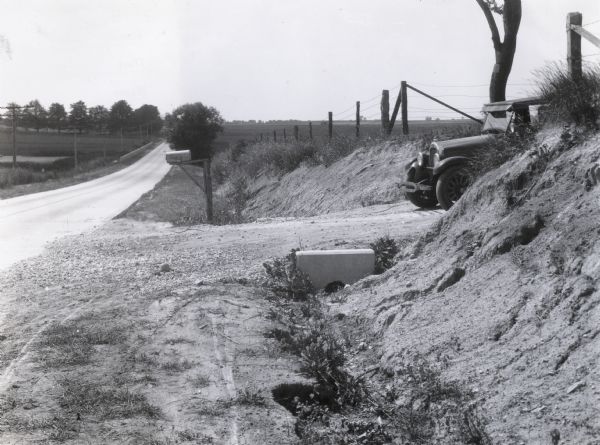 An automobile driving down a driveway between two embankments, prohibiting a clear view of an intersecting road.