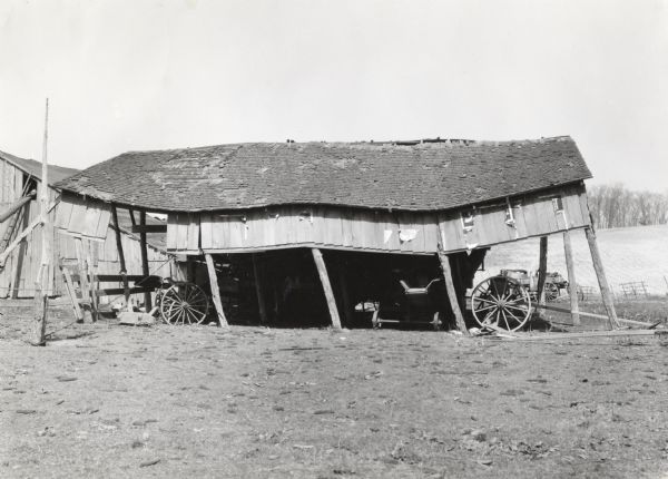A collapsing shed housing various pieces of farm machinery and wagons.