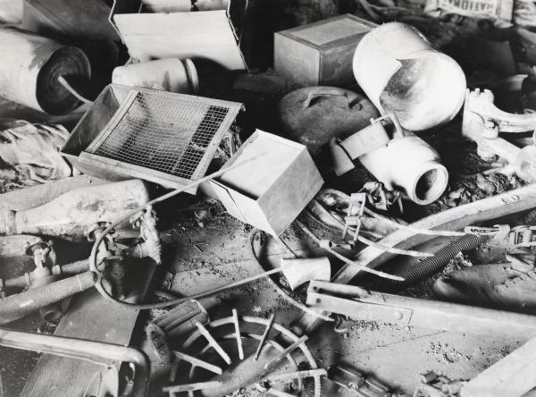 Close-up view of a pile of garbage in a farmhouse attic consisting of metal pieces, pipes, machine parts, and other items.
