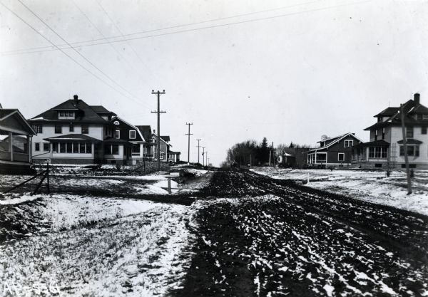 View down a snow-covered dirt road surrounded on either side by retired farmer residences.