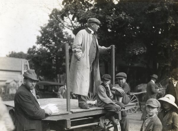 C.H. Allen stands on the back of a wagon to address a group on the subject of alfalfa. Men and boys stand around him to listen.