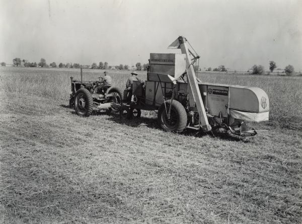 Three-quarter rear view from left of a McCormick-Deering No. 22 harvester thresher (combine) operating in a field. Original caption reads: "Combining soybeans on the Purdue University Soils and Crops farm near Lafayette, Indiana, using Firestone equipped McCormick-Deering Model 22 combine and F-20 Tractor." Decals and/or stencils are on the machine.