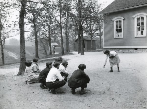 Children play a game outdoors beside a rural school building.