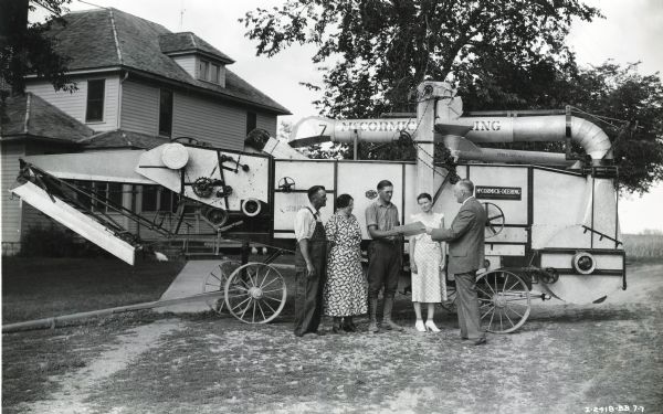 Merton Sutter receiving a 4-H farm accounting award in front of a McCormick-Deering All-Steel Thresher. Original caption reads: "Winner of $300 merchandising certificate in 1937 National 4-H Farm Accounting Contest. Merton is being congratulated by W.R. Ploetz, branch manager, Madison, Wis."