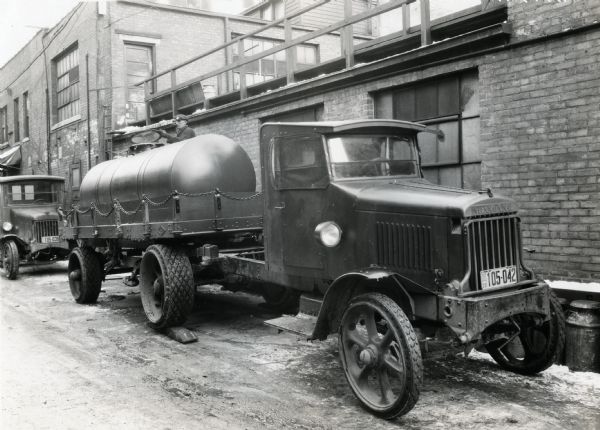 A Model 94 International truck and trailer owned by the Risdon Creamery Company parked alongside a brick building.