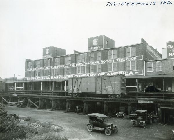 An elevated railroad passes by International Harvester's Indianapolis branch office. Signs painted on the building advertise "Threshers, Plows, Farm Machines, Oil Tractors and Engines, Wagons, Motor Trucks."
