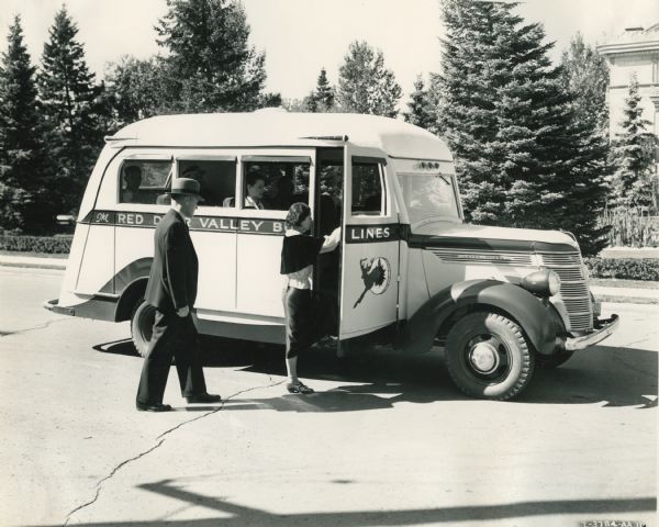 A nicely dressed woman and man (couple?) boarding an International D-15 12-passenger bus owned by W.H. Rounds, Red Deer Valley Bus Lines.