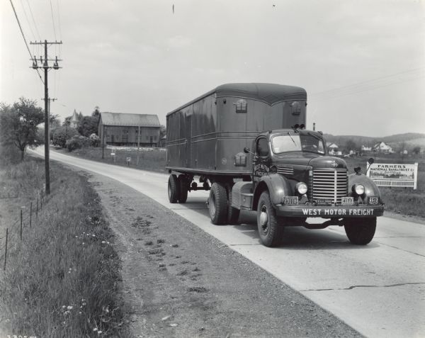 Man driving an International KR-11 truck with semi-trailer (semi-truck) on a rural highway. The truck was owned and operated by West Motor Freight of Boyertown, Pennsylvania.