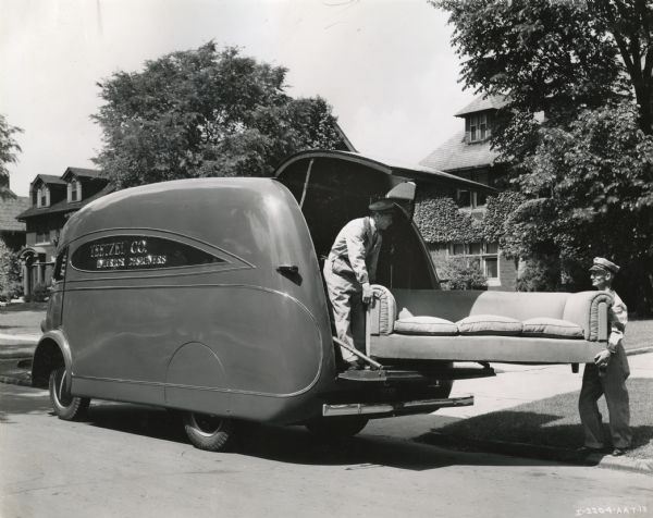 View from street of two men removing a sofa from the back of an International D-30 truck owned by Teetzel Company Interior Designers.
