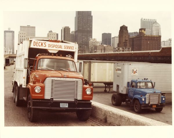 Color photo of an International Fleetstar truck outfitted with a garbage hauler. The truck was owned by Deck's Disposal Service and appears against a background of skyscrapers; a building marked "310 W. Polk Building" appears at right.