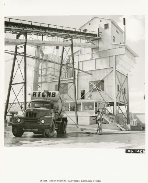 Atlas Concrete Products Truck An International truck owned by Atlas Concrete Products, Inc. parked in front of industrial buildings. A man is standing on the right hosing off the truck. In the background another man is in a glassed-in office at the base of a tall industrial tower.