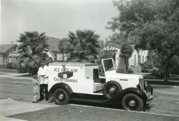 The driver of a Good Humor ice cream truck sells ice cream to a young customer in a residential neighborhood.