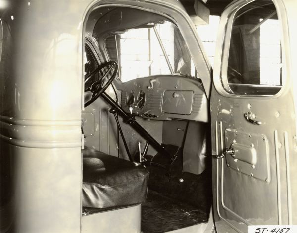 Interior of a International Harvester Model Truck Interior view through open passenger side door of an International Harvester model truck, showing steering wheel and column, seat, dashboard, windshield, and door panel. Possibly a Raymond Loewy design.