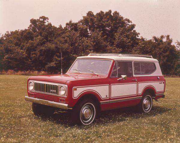 Scout II Traveltop Parked Outdoors Three-quarter view from front of driver's side of red Scout II. White detailing on sides, white traveltop. Parked outdoors in a field, trees in the background.