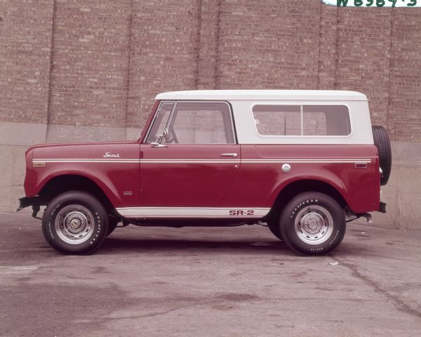 Scout SR-2 Parked Outdoors Driver's side view of red Scout SR-2 with white top parked outdoors in front of a brick building. Spare tire is mounted on the back.