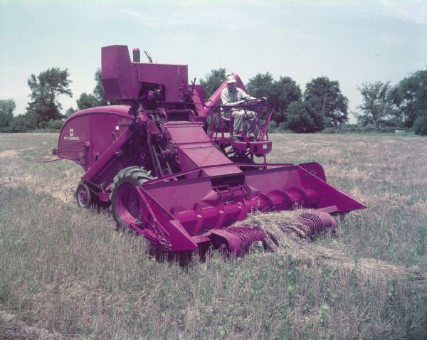 Man using a 127 SP combine in a field Three-quarter view from right front of man operating a McCormick 127 SP combine in a field.