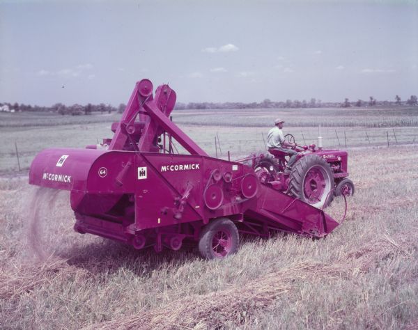 Man using Farmall M to pull a McCormick 64 combine in field Three-quarter view from right rear of a man in a field operating a Farmall M tractor to pull a McCormick 64 combine.