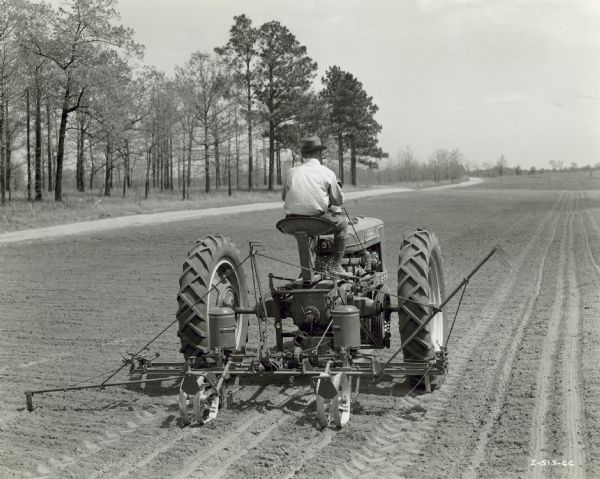 Farmall H Tractor with H-100 Corn Planter Rear view of a man driving a Farmall H tractor with H-100 corn planter in a field.