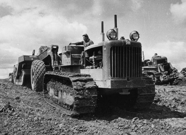 TD-24 Torque Converter Tractor Original caption reads: "TD-24 Torque Converter Tractor push loads a 24 and B-250 27 /12 hd. scraper combination in hard fire clay whilst a gear driven-24 and Ateco Ripper work in the background."