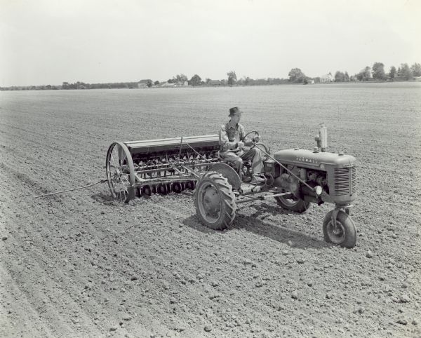 Farmall B Tractor Slightly elevated three-quarter view from front right of Ray Whetstone drilling soybeans with Farmall B tractor and 13-7 McCormick-Deering fertilizer drill.