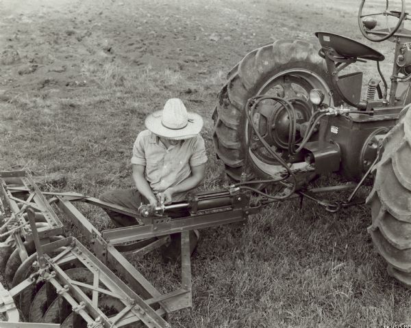 Man Working on Farmall M Tractor Man working on Farmall M tractor and 8 foot No. 10A disk harrow equipped with remote control hydraulic cylinder.