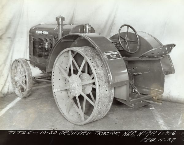 McCormick-Deering 10-20 Orchard Tractor Three-quarter view from left rear of McCormick-Deering 10-20 tractor. There is cloth canvas hung in the background as a backdrop. Original caption reads: "Title — 10-20 Orchard Tractor. Neg. No. G.P. 11916 Feb 5-37."