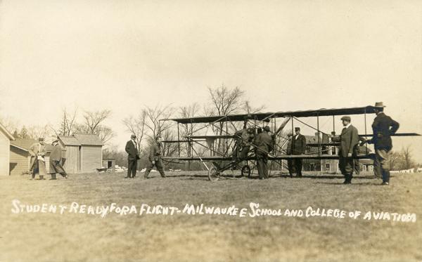 An unidentified student among a group of men getting a lesson in a Curtiss plane at Rudolph Silverston's Milwaukee School and College of Aviation. Caption reads: "Student ready for a flight — Milwaukee School and College of Aviation." 