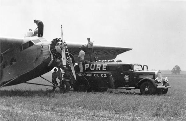 Refueling a Ford Tri-Motor airplane. Because gasoline truck hoses did not have pumps, airplanes were refueled by filling 5-gallon cans and then lifting the cans up to the fuel tank. The fuel was then siphoned through a chamois cloth to remove impurities.