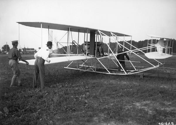 Wilbur Wright, in the bowler hat, preparing the Flyer for the conclusion of the test required to win a U.S. Army contract. The 1908 demonstration had been interrupted by a crash in which Orville was seriously injured and his passenger killed. This photograph shows clearly the track from which the early Flyers were catapulted and Wilbur's intense concentration.