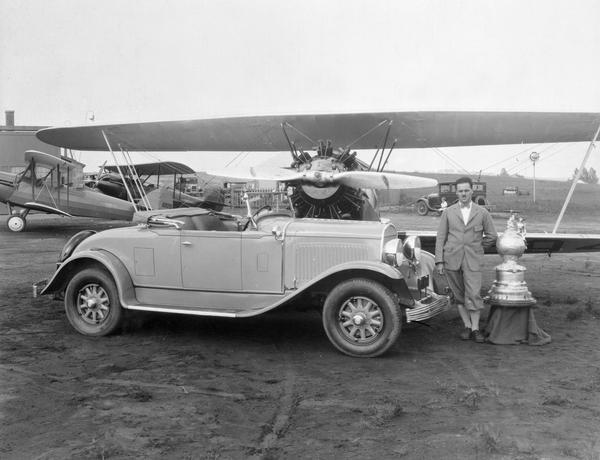 John P. Wood of Wausau, winner of the 1928 National Air Reliability Tour, with his "Waco from Wausau." Also in the photograph are Wood's prizes: the Edsel B. Ford Trophy and a new Chrysler automobile.