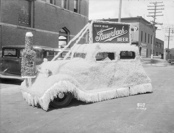 An automobile covered in crepe paper with a beer bottle on the front end, and a sign on the top serves as the Fauerbach Brewing Co. float. It was built to be in a parade celebrating the opening of Park and Regent Streets. Taken in front of the Fauerbach building, the Madison Drug Company at 654 Williamson Street.