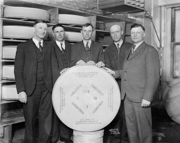 Five men stand behind a 200 pound wheel of Swiss cheese. Written on wheel is "Madison Milk Producers Cooperative Ass'n." The cheese was a gift for Major Edward Bowes for featuring Madison on his radio amateur talent show. 29 Coyne Ct.