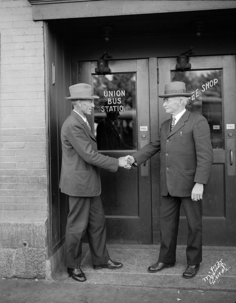 George A. Nelson, Milltown, former assemblyman and president of the Wisconsin Union of the American Society of Equity, and John E. Cashman, Denmark, State Senator, shaking hands in front of the Union Bus Station.