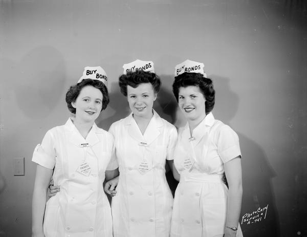 Three female employees of Rennebohm Drugstore #2, 204 State Street, wearing white  uniforms, caps and neckties with slogans urging people to buy war bonds: "Third Party, Private, Fifth War Loan, Retailers for Victory."