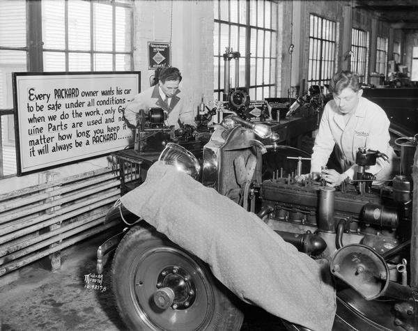 At Gabbei Motor Co. at 412 East Washington Avenue, one man works on the engine of a car while another machines a part in the company garage.