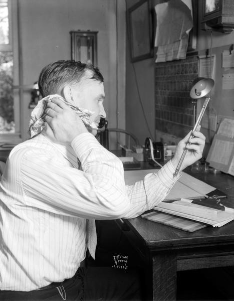 U.S. weather observer, Oscar E. Olson, sitting at his desk, looking at a thermometer and wiping the sweat from the back of his neck on a hot summer day.