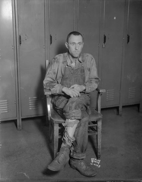 Chester Briggs, aka Chester Hawk or John Stanovich, was found by police in a boxcar at the Milwaukee Road switching tracks. He is sitting in a chair at the police station, wearing an iron shackle on his left leg.
